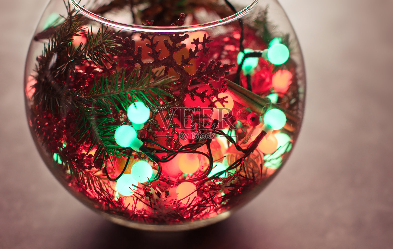 圣诞背景:灰色抽象背景上有一个圆形玻璃鱼缸，上面有橘子、云杉树枝、花环和红色的节日装饰品照片摄影图片