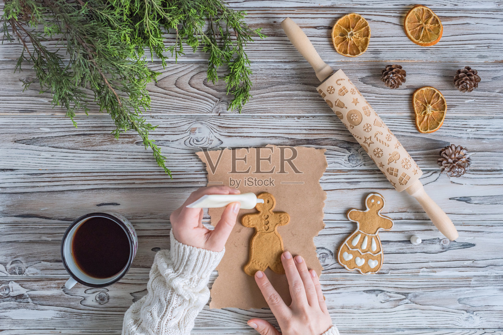 女人把蜂蜜姜饼装饰在木制的灰色桌子和牛皮纸上。圣诞糖衣面包店。平躺照片摄影图片