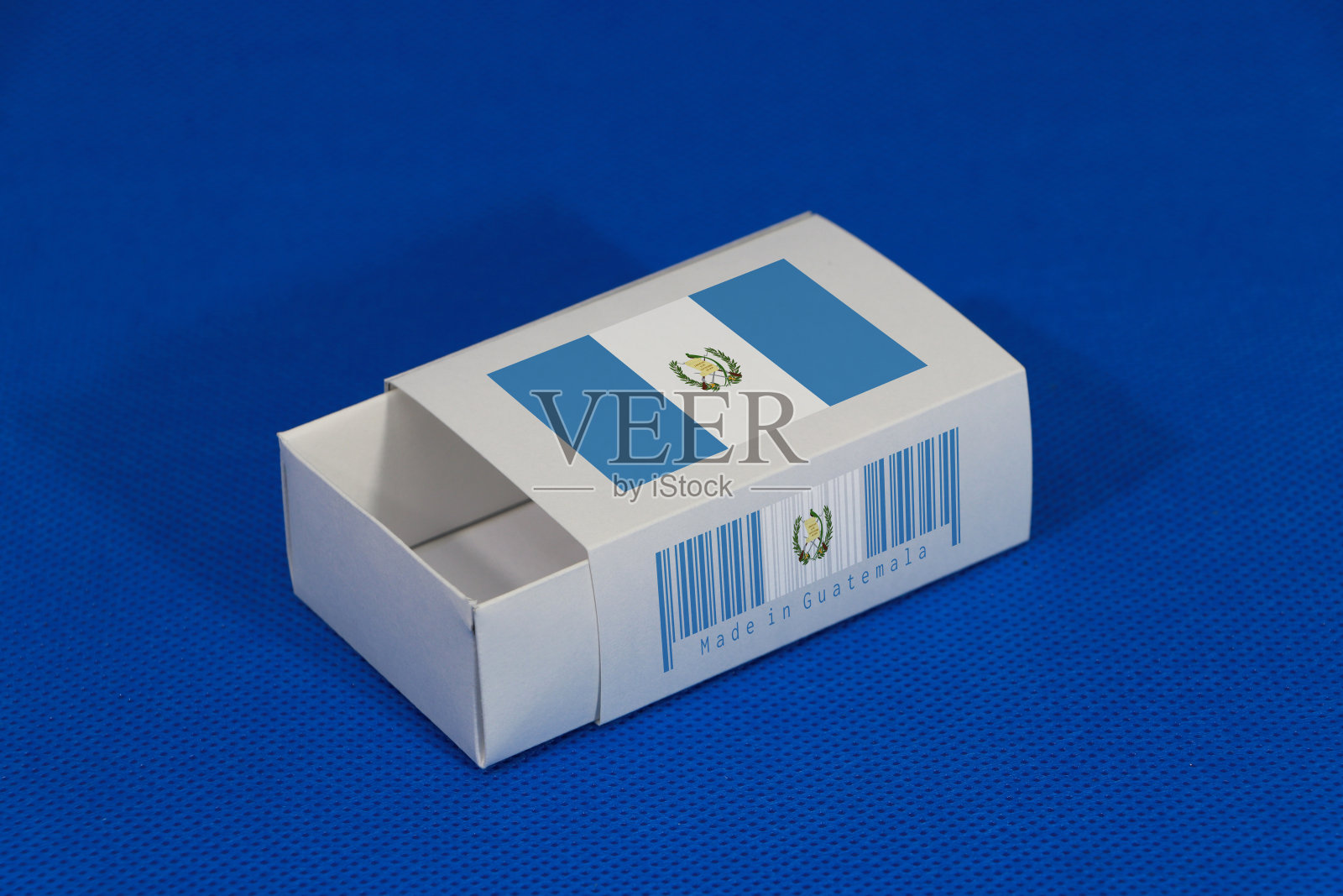 危地马拉国旗上的白色盒子与条形码和颜色的国旗上的蓝色背景，纸包装放火柴或产品。出口贸易的概念。照片摄影图片