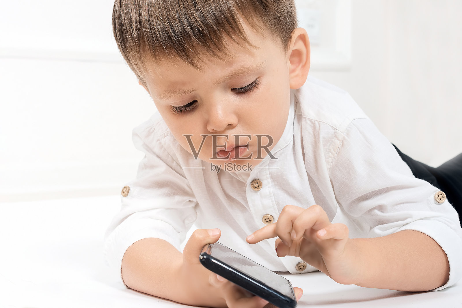 一个长着欧洲面孔的小男孩，手里拿着一部智能手机。网瘾的概念与年轻一代的现代教育。放置你的文本。照片摄影图片