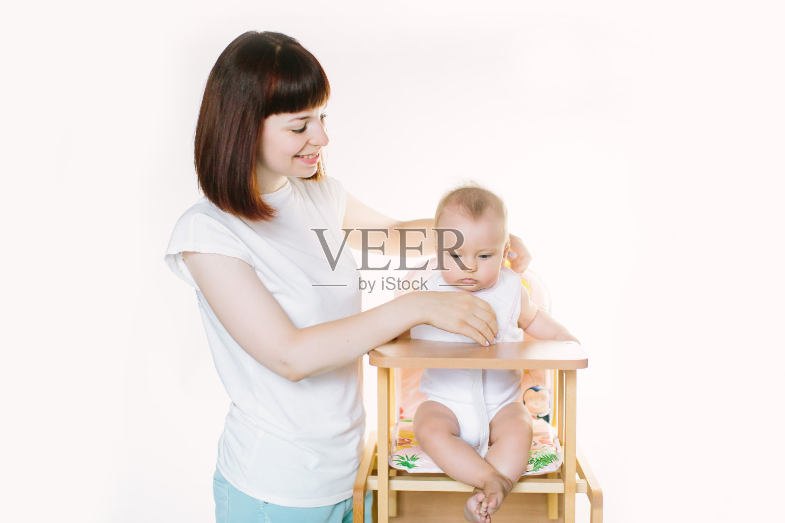 年轻美丽的母亲给她的小女儿戴上白色围嘴，她坐在椅子上。照片摄影图片