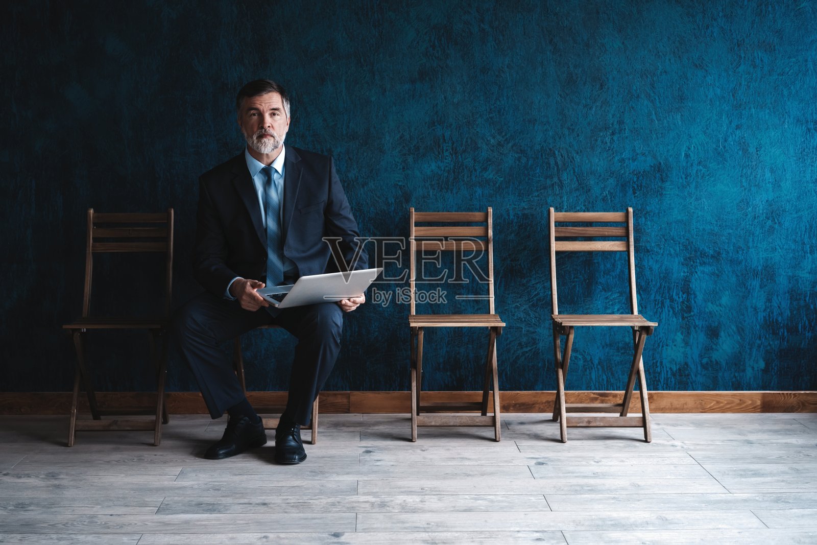 等待面试。在深蓝色的背景下，自信成熟的商人坐在椅子上。照片摄影图片