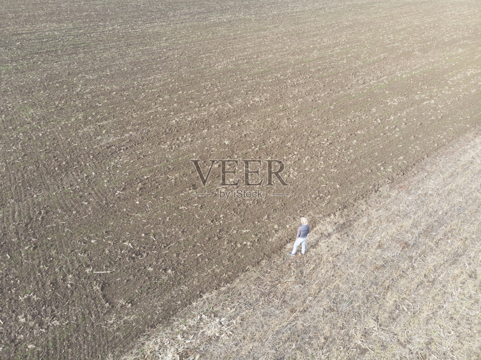 在秋天，成年农民戴着牛仔帽站在他犁过的农田旁边。鸟瞰图。照片摄影图片