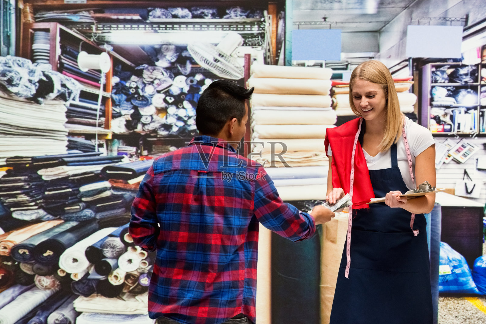 一人/腰部以上/两人金发女/年轻女/男性朋友/客户/销售职业/纺织商/女商人/手工艺人/裁缝站在布艺店的店里/穿围裙的服装店照片摄影图片