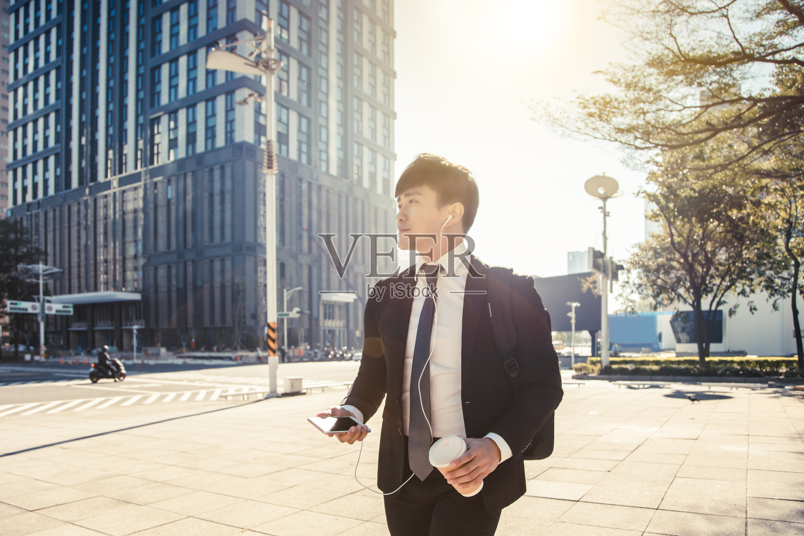 商人拿着手机走在去办公室的路上照片摄影图片