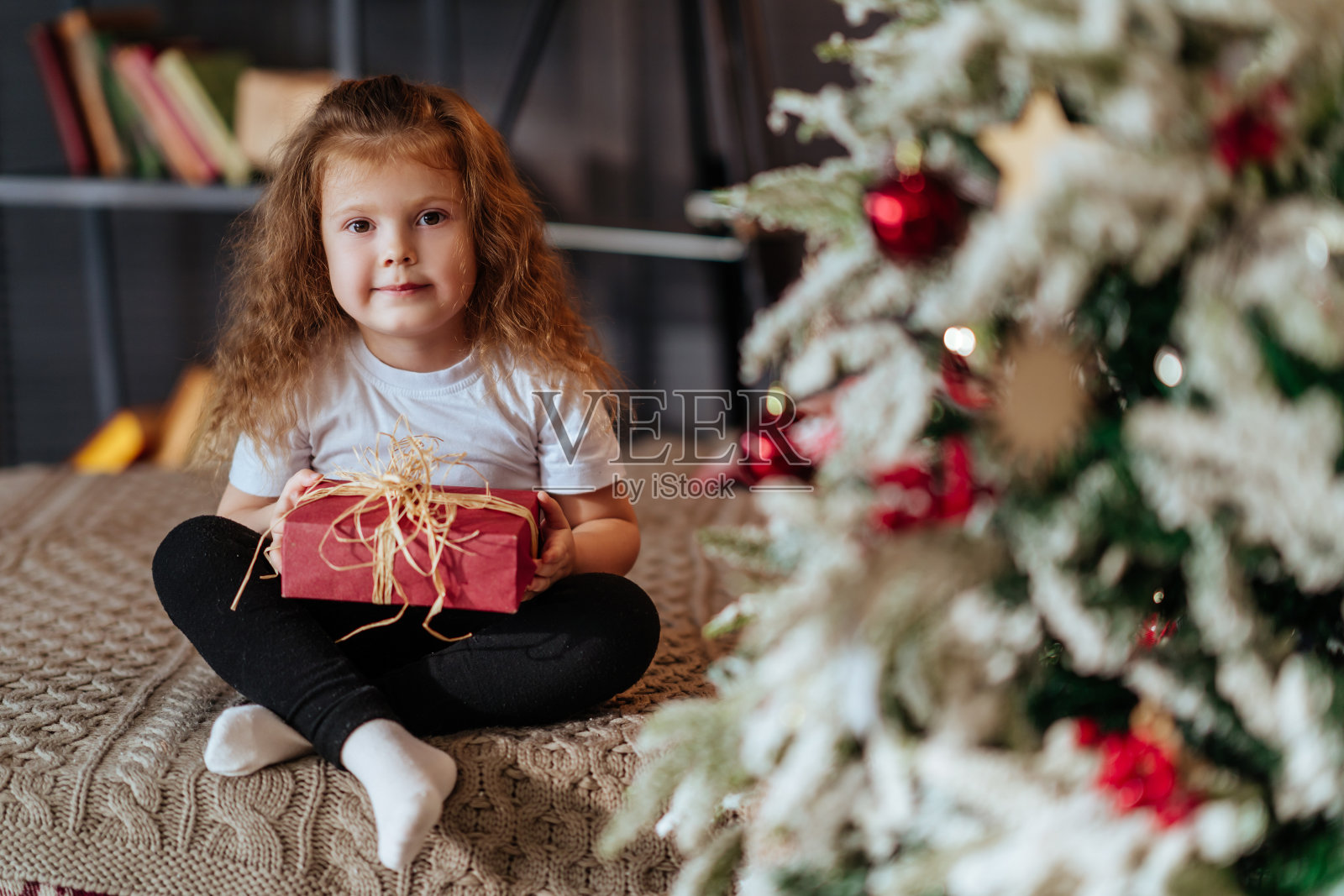 在新年圣诞树的背景下，一个孩子坐在床上照片摄影图片