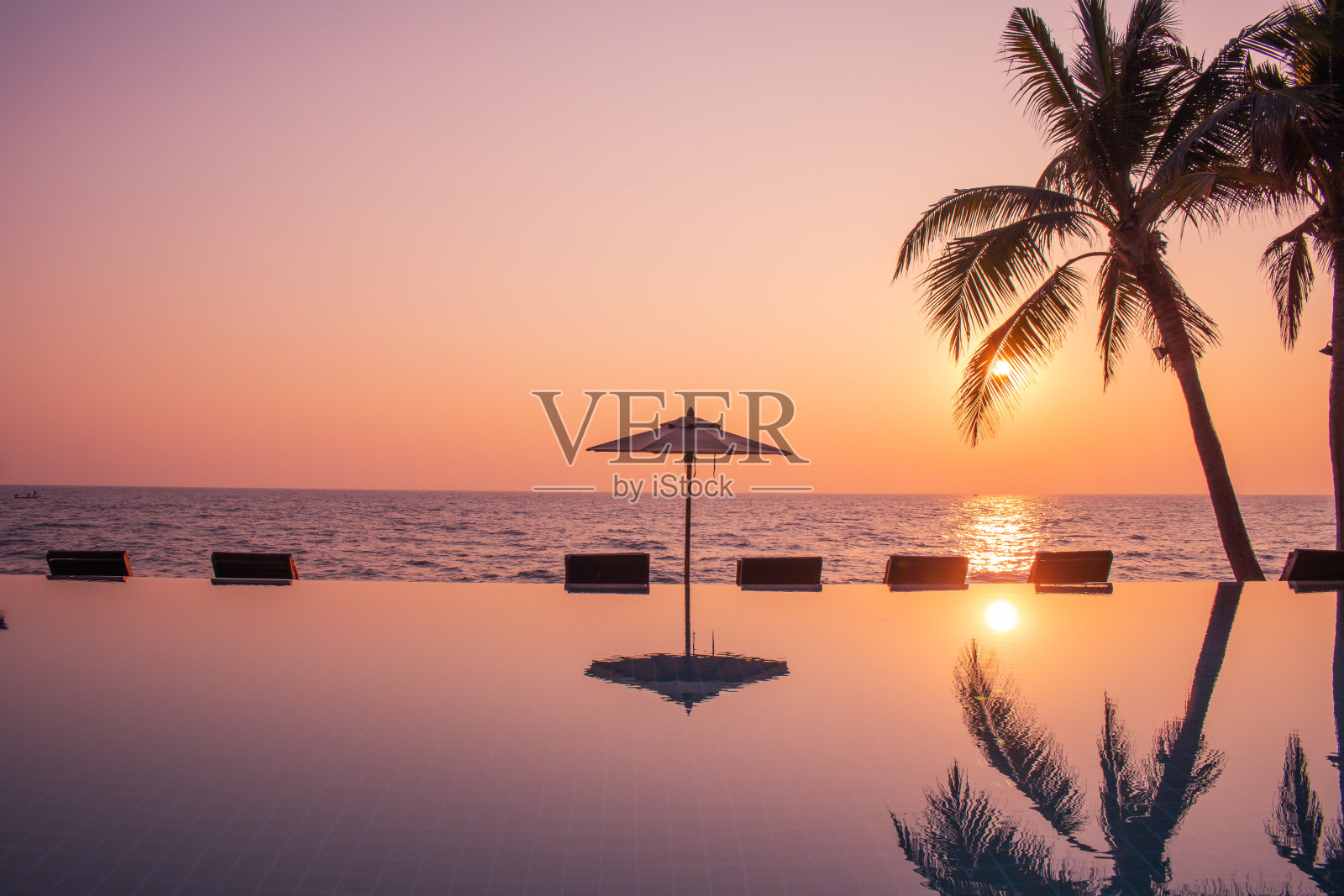 在日出的背景下，剪影沙滩伞和椰子树。照片摄影图片