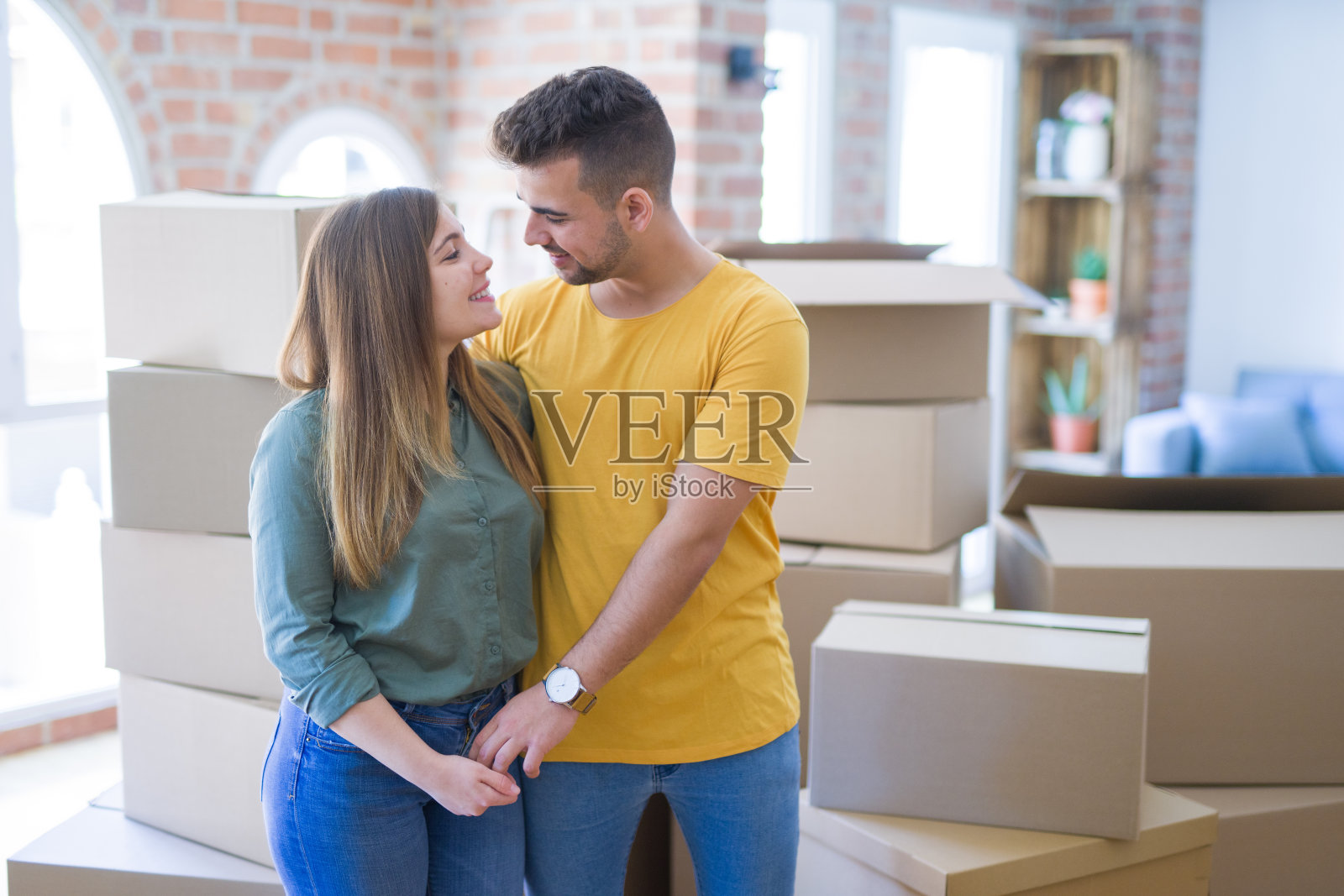 年轻美丽的情侣围绕着纸箱搬到新家，笑得很开心，欢天喜地的搬到新公寓照片摄影图片