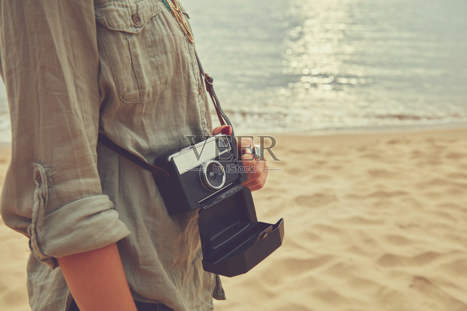 海滩上拿着相机的时尚女人。照片摄影图片