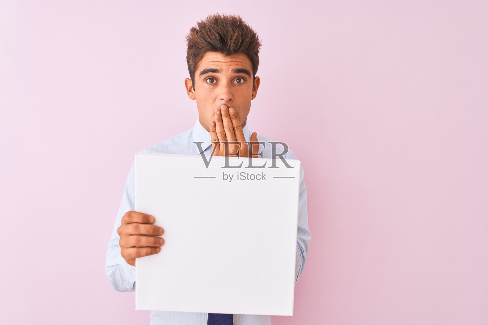 年轻英俊的商人举着横幅站在孤立的粉红色背景上捂着嘴，用手为错误而震惊，表情恐惧，默默的害怕，秘密的概念照片摄影图片