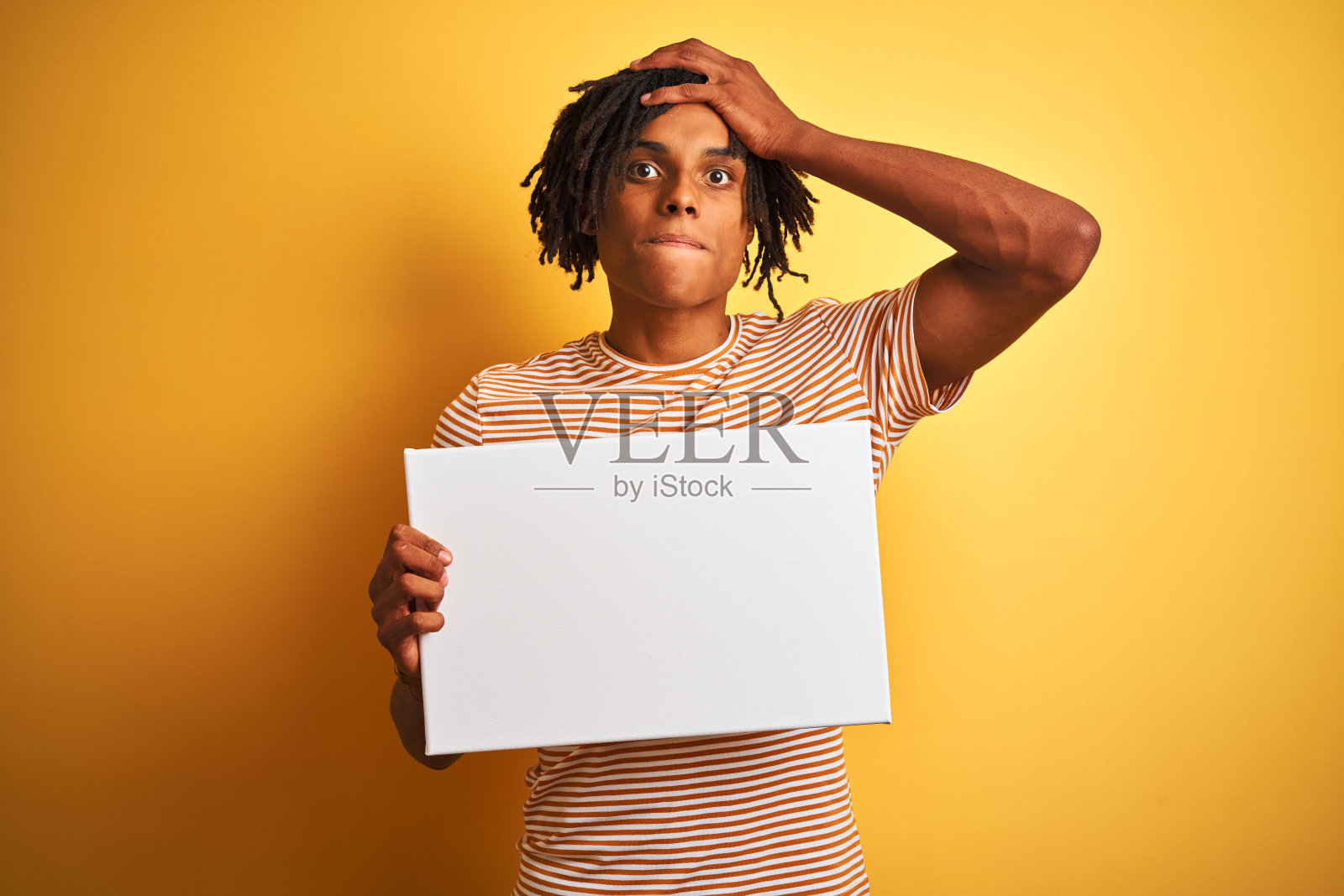 非裔美国人，长着发辫，高举旗帜越过孤立的黄色背景，强调用手顶着头，因羞愧和惊讶而震惊，愤怒和沮丧。为错误而恐惧和不安。照片摄影图片