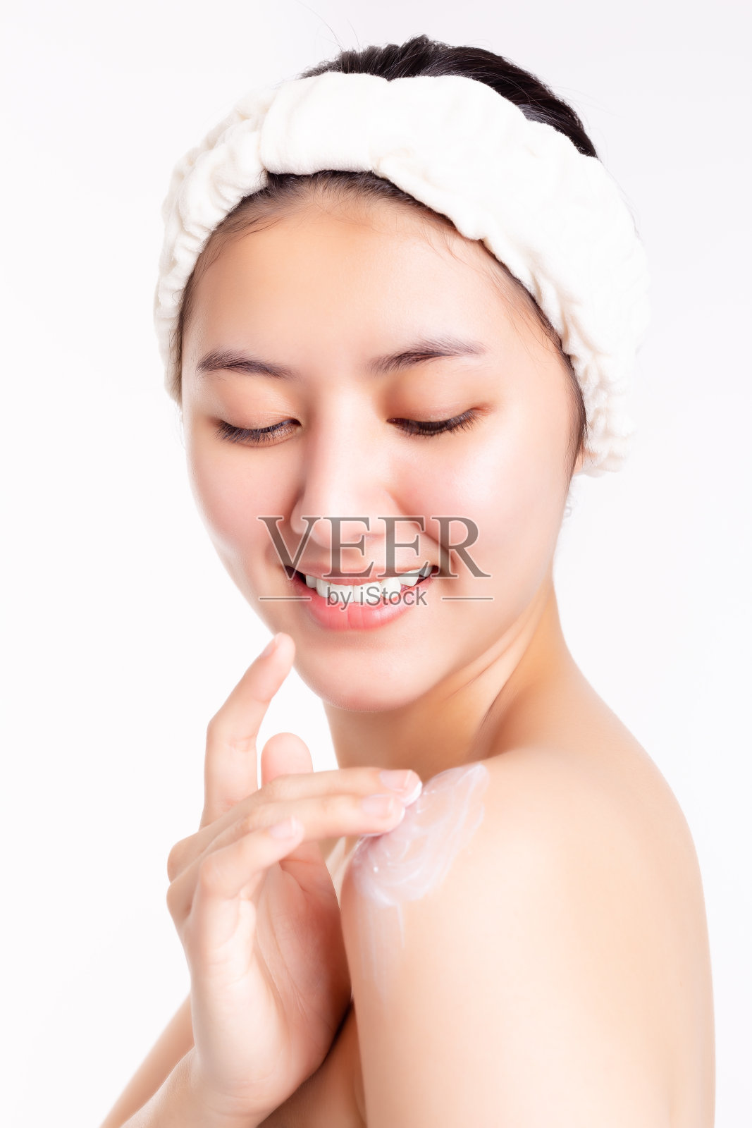 亚洲女性把霜或润肤霜，以美容身体或增加水分，她的皮肤。美丽的年轻亚洲女士有漂亮的皮肤和美丽的脸与笑脸。在白色背景上隔离照片摄影图片