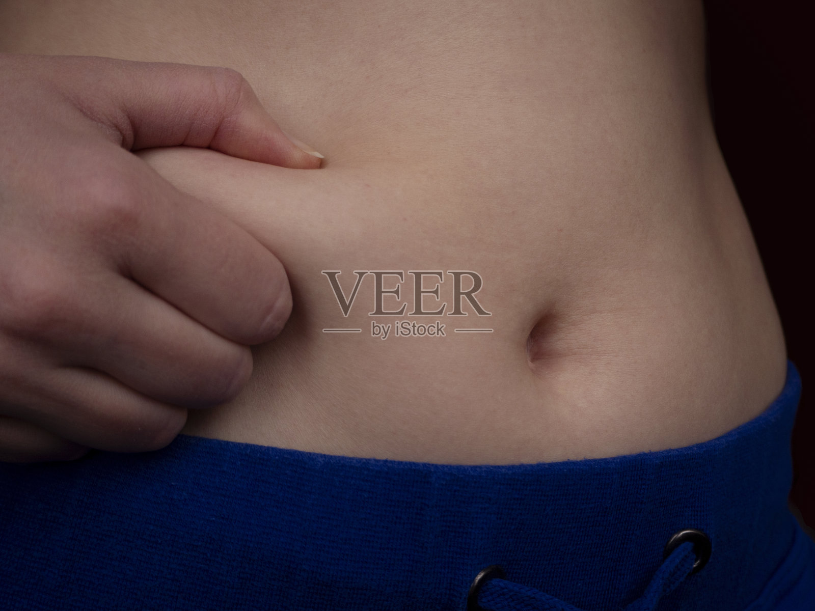 女性腹部有多余的脂肪。一个开始增加体重的年轻白人妇女用右手挤压她腰部的脂肪。照片摄影图片