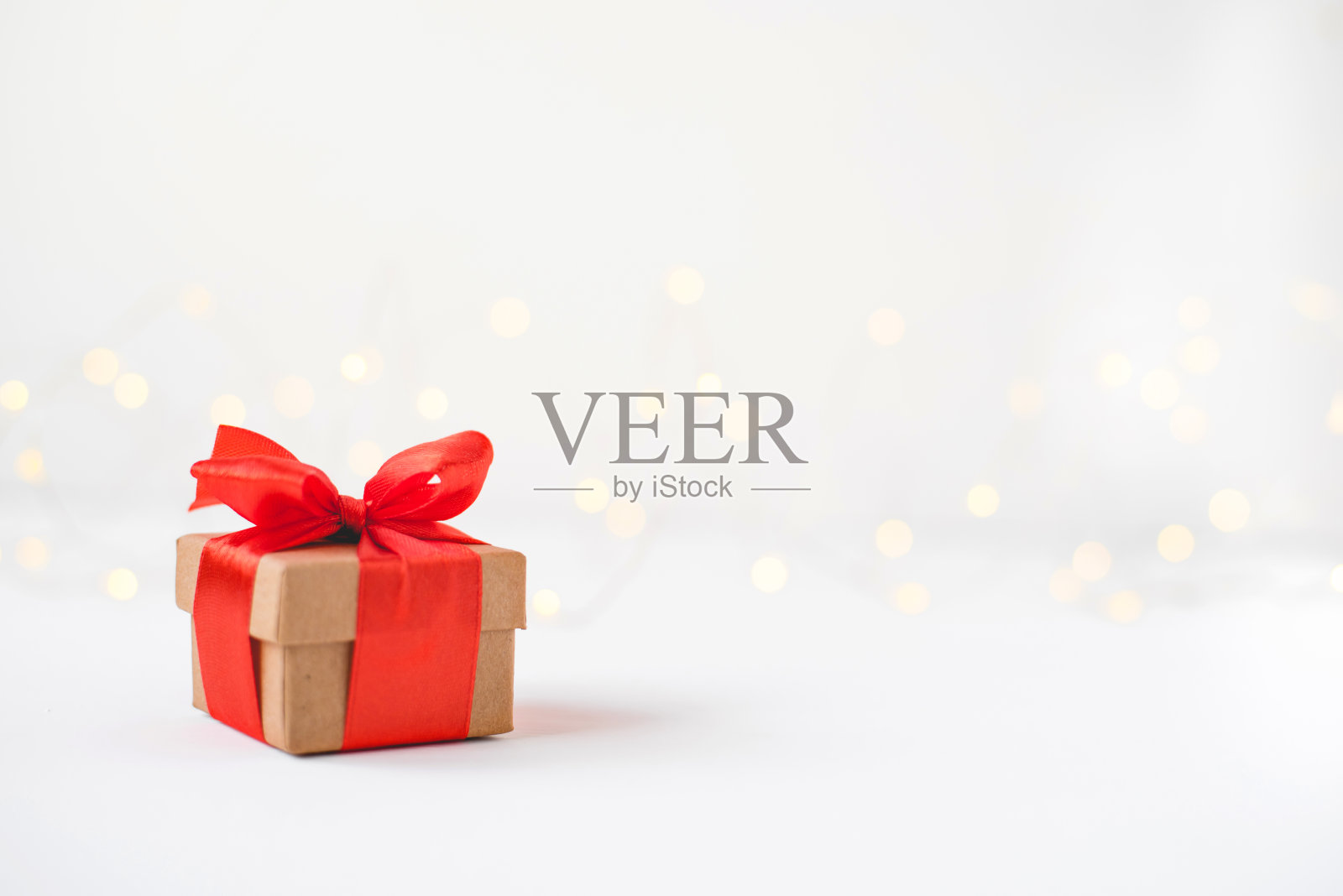 礼盒与一个红色的蝴蝶结在背景模糊的灯光花环。照片摄影图片