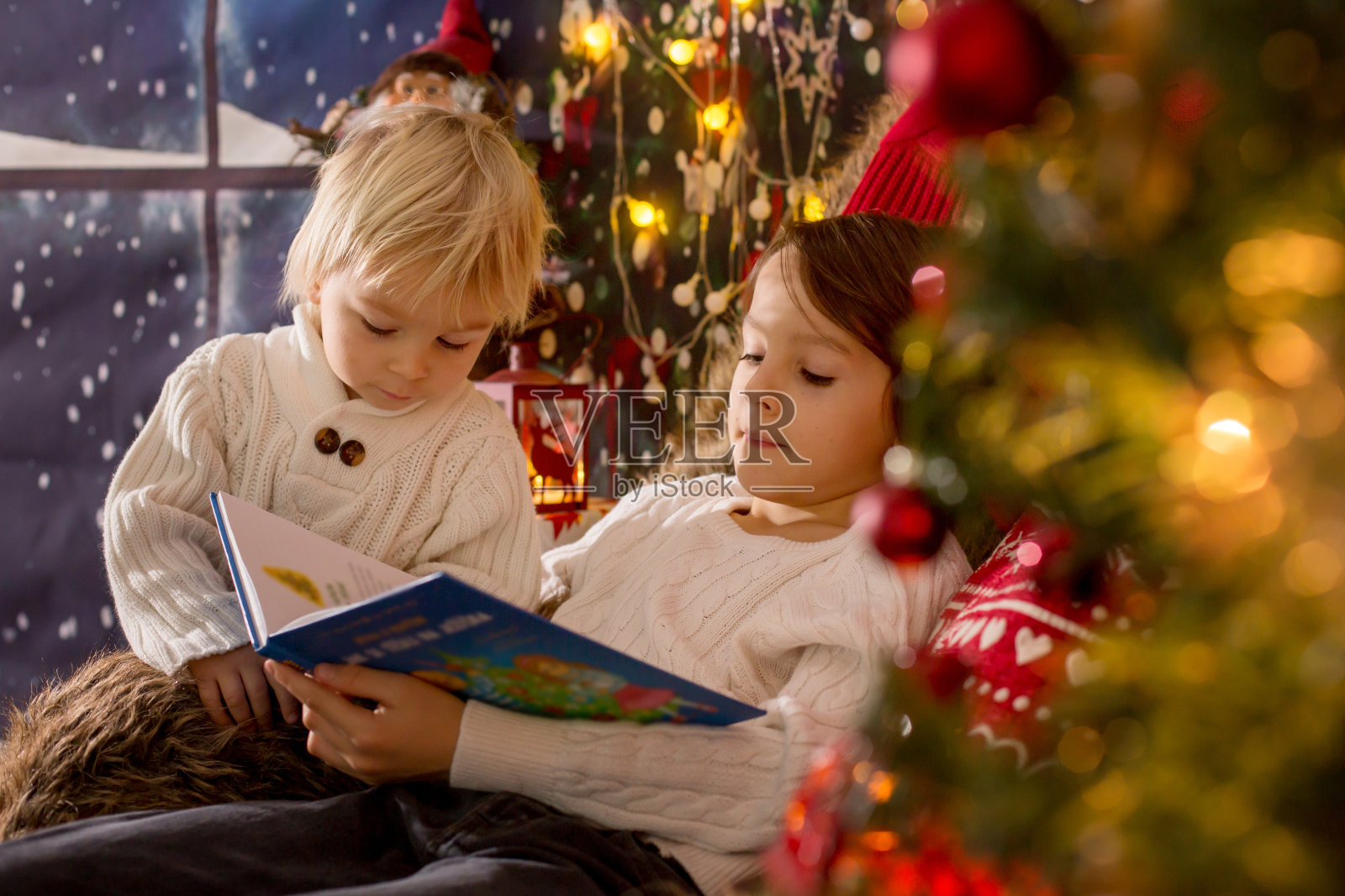 可爱的小男孩和哥哥，坐在圣诞树旁舒适的椅子上看书照片摄影图片