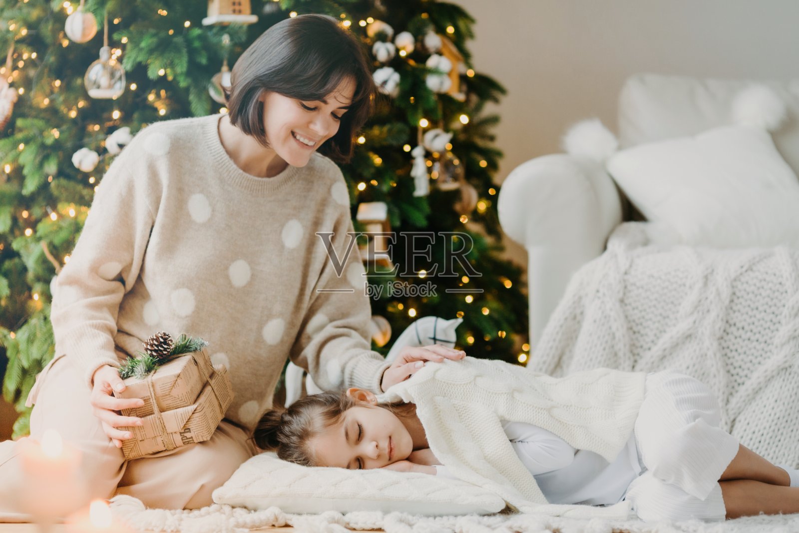 在家庆祝圣诞节。漂亮年轻的妈妈叫醒小孩子，说该打开礼物了，对着装饰好的新年树摆姿势，在舒适的客厅摆姿势。传统的家庭假期照片摄影图片