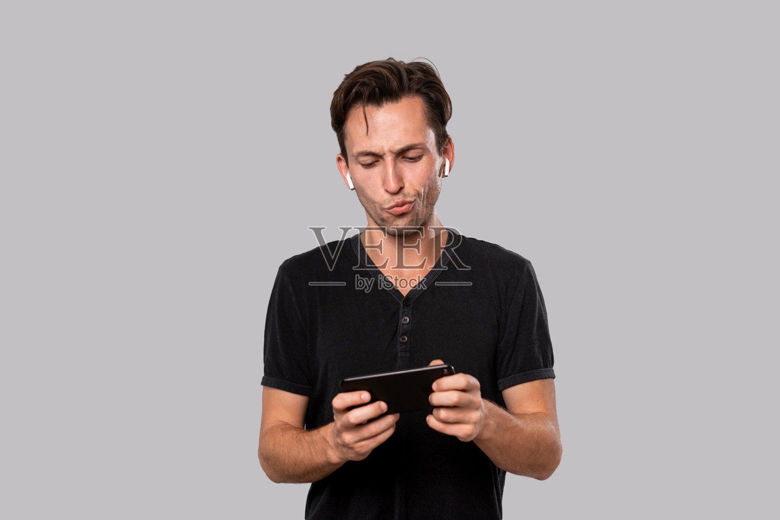 年轻英俊的男人拿着无线耳机拿着智能手机。照片摄影图片