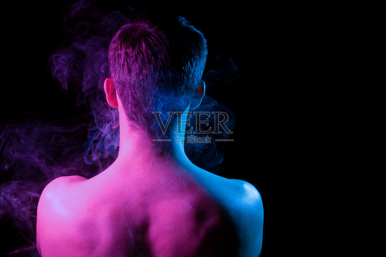 近距离特写一个留着短头发的男人的头，他有胡茬，赤裸着衣服，用蓝色和粉色照亮了一个黑色孤立的背景和烟雾照片摄影图片