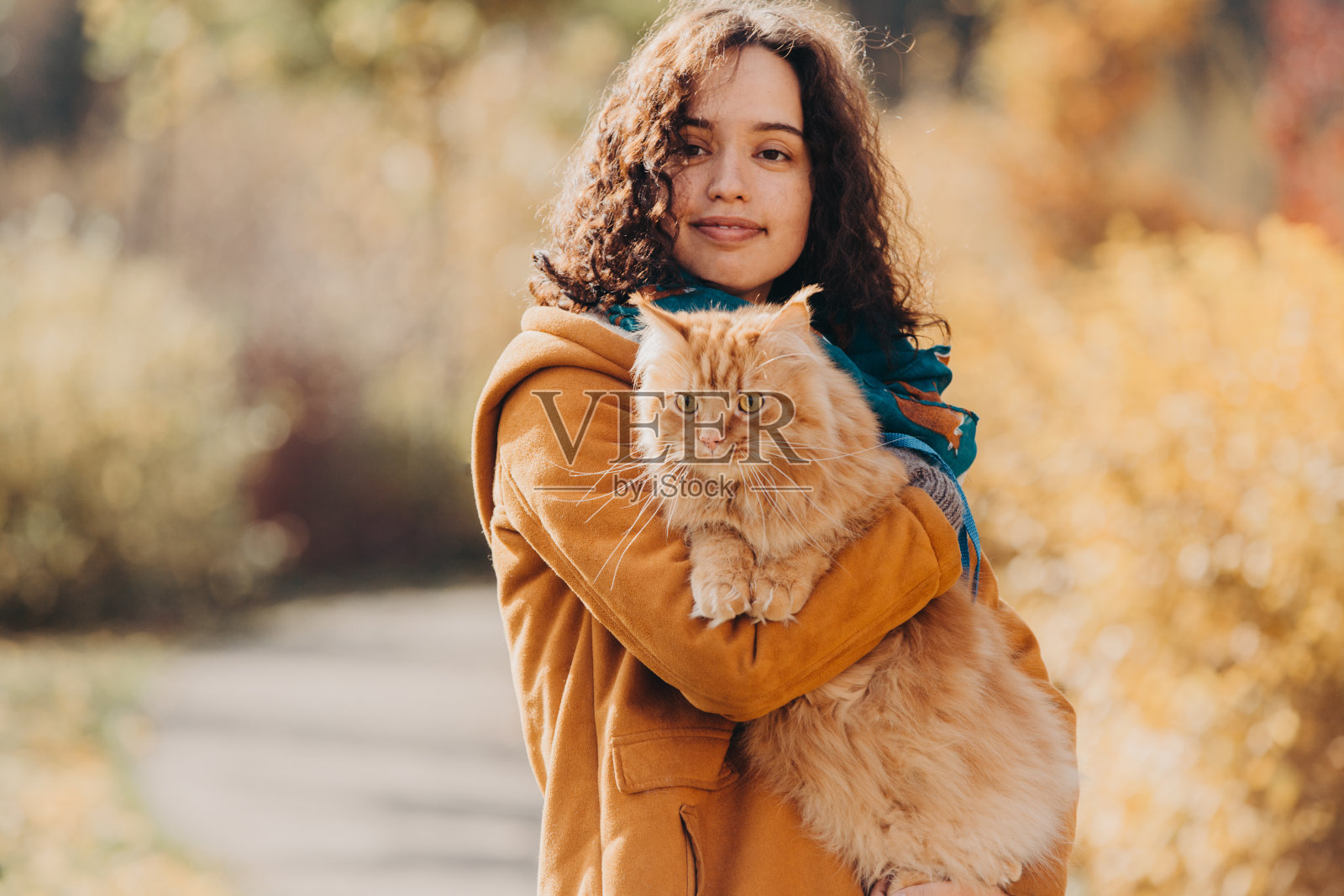 一个女孩和一只红猫走在秋天的街道上。照片摄影图片