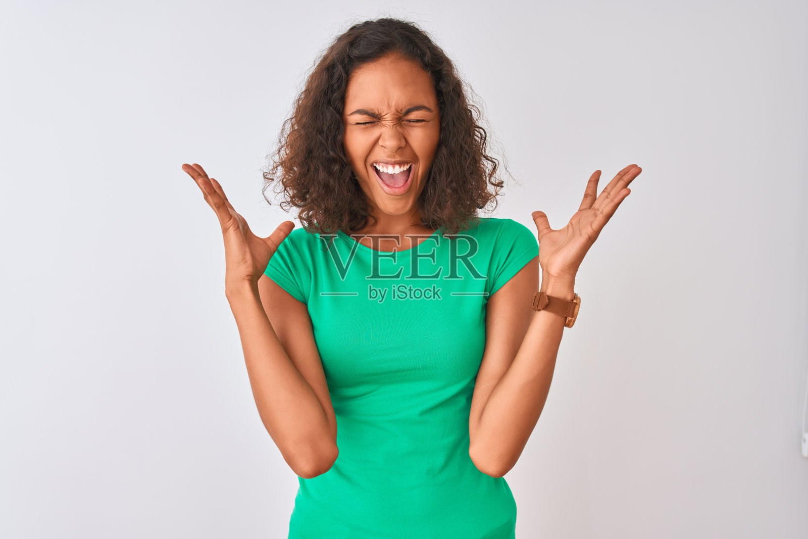 一名年轻的巴西女子身穿绿色t恤站在孤立的白色背景下，高举双臂，闭上眼睛兴奋地尖叫，为成功而疯狂。赢家的概念照片摄影图片