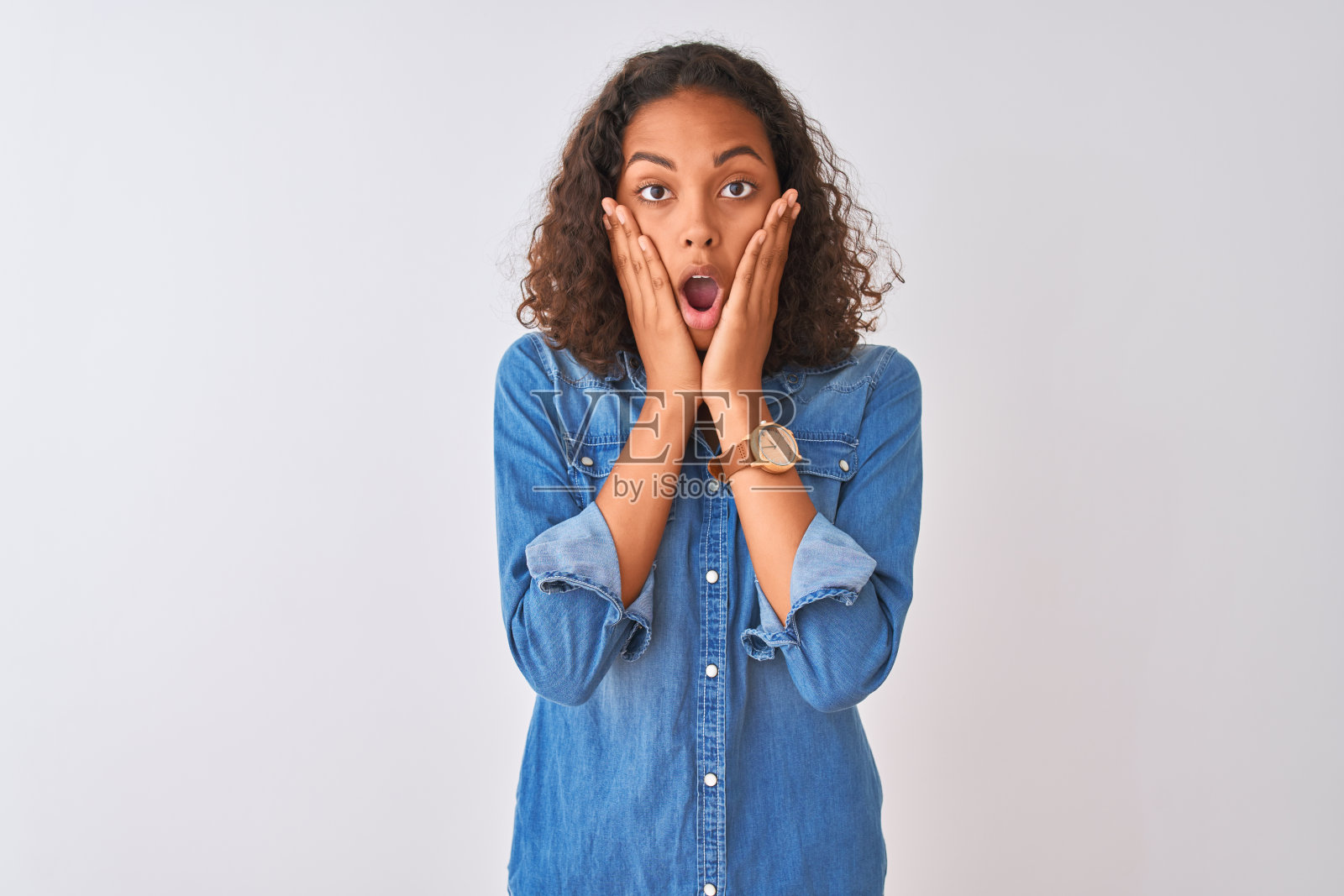 年轻的巴西女人穿着牛仔衬衫站在孤立的白色背景害怕和震惊，惊讶和惊讶的表情与手在脸上照片摄影图片