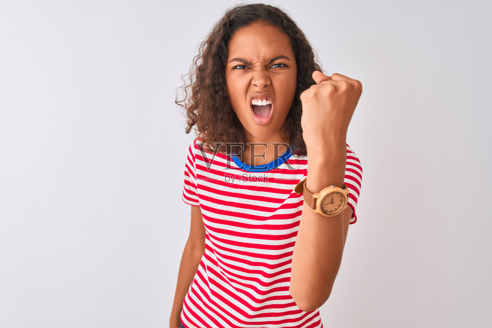 年轻的巴西女子穿着红色条纹t恤站在孤立的白色背景愤怒和疯狂举起拳头，沮丧和愤怒，同时大喊着愤怒。愤怒和侵略性的概念。照片摄影图片