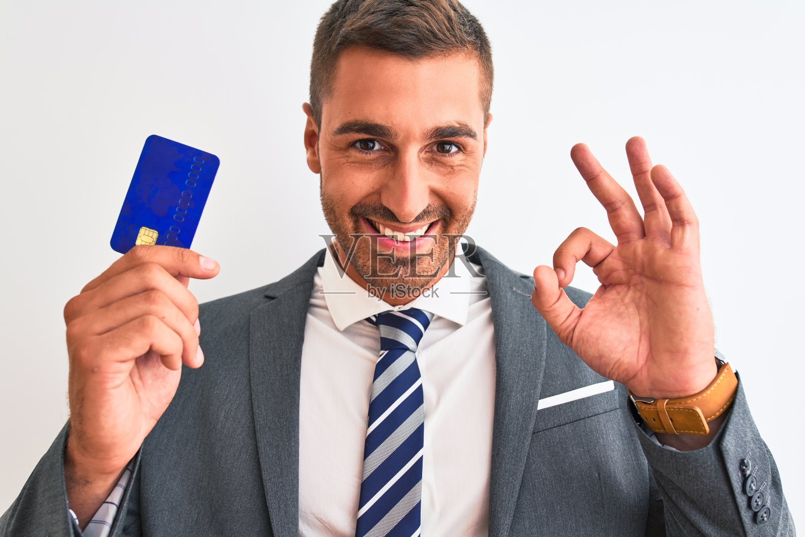 年轻英俊的商人拿着信用卡在孤立的背景做ok手势用手指，优秀的象征照片摄影图片