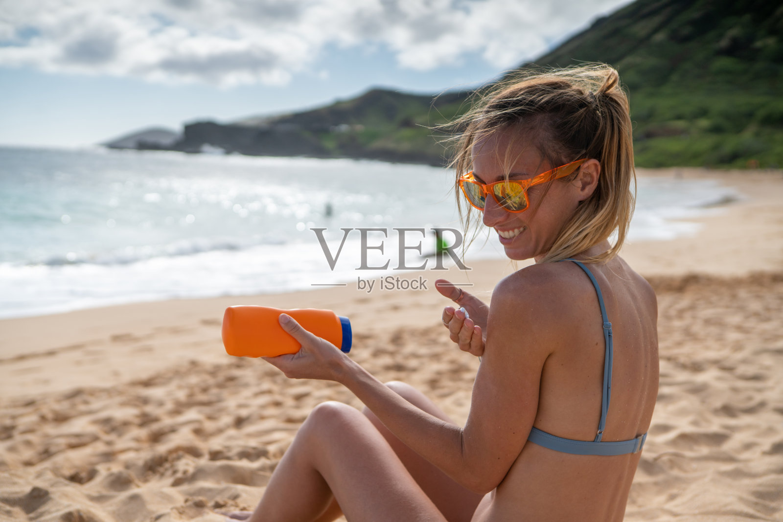 夏日——年轻女子在海滩上涂抹防晒霜，保护皮肤照片摄影图片