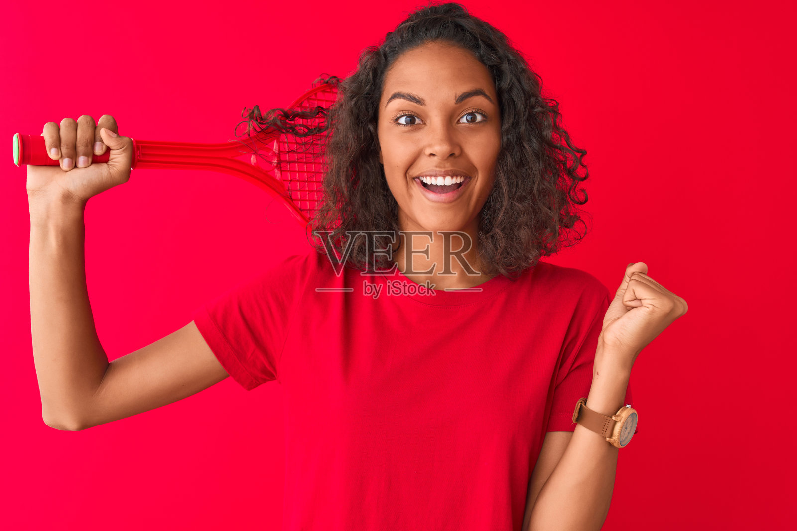 年轻的巴西女运动员拿着网球拍站在孤立的红色背景尖叫自豪，庆祝胜利和成功非常兴奋，欢呼的情绪照片摄影图片