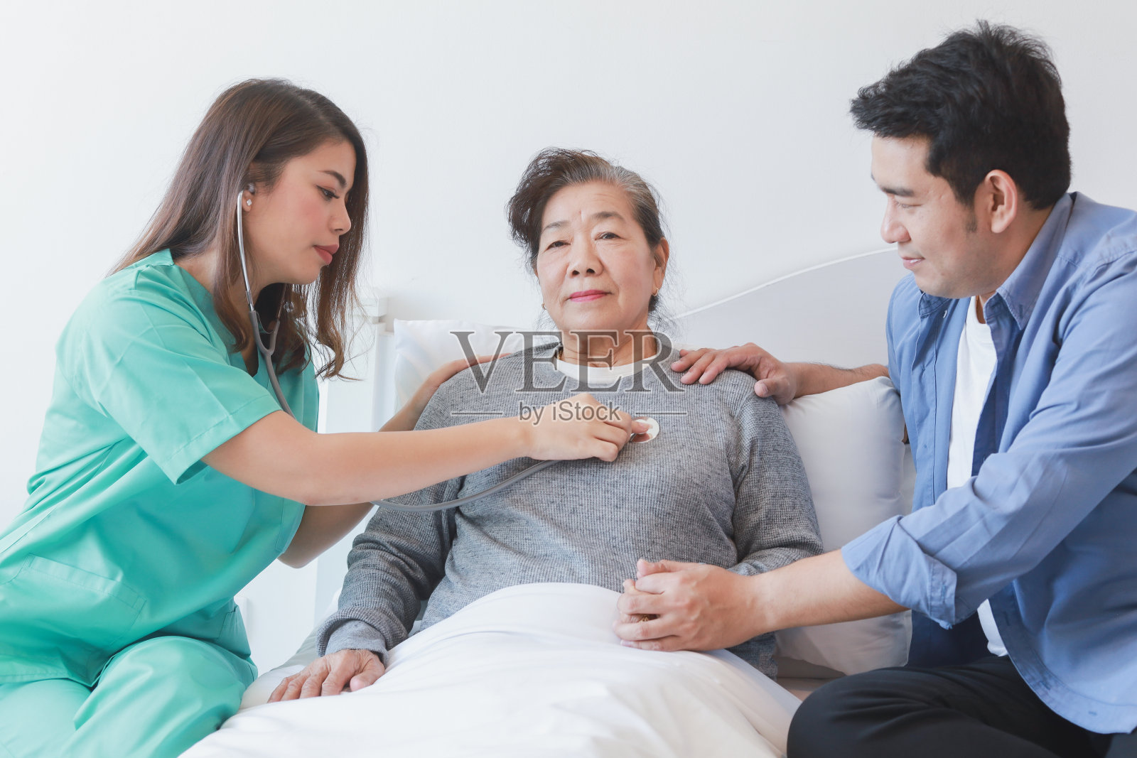 一位老年妇女躺在病床上，医生和她的儿子在医院里照片摄影图片