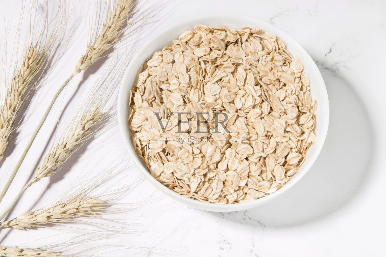 干燕麦片在盘子里，小麦穗在白色的背景照片摄影图片