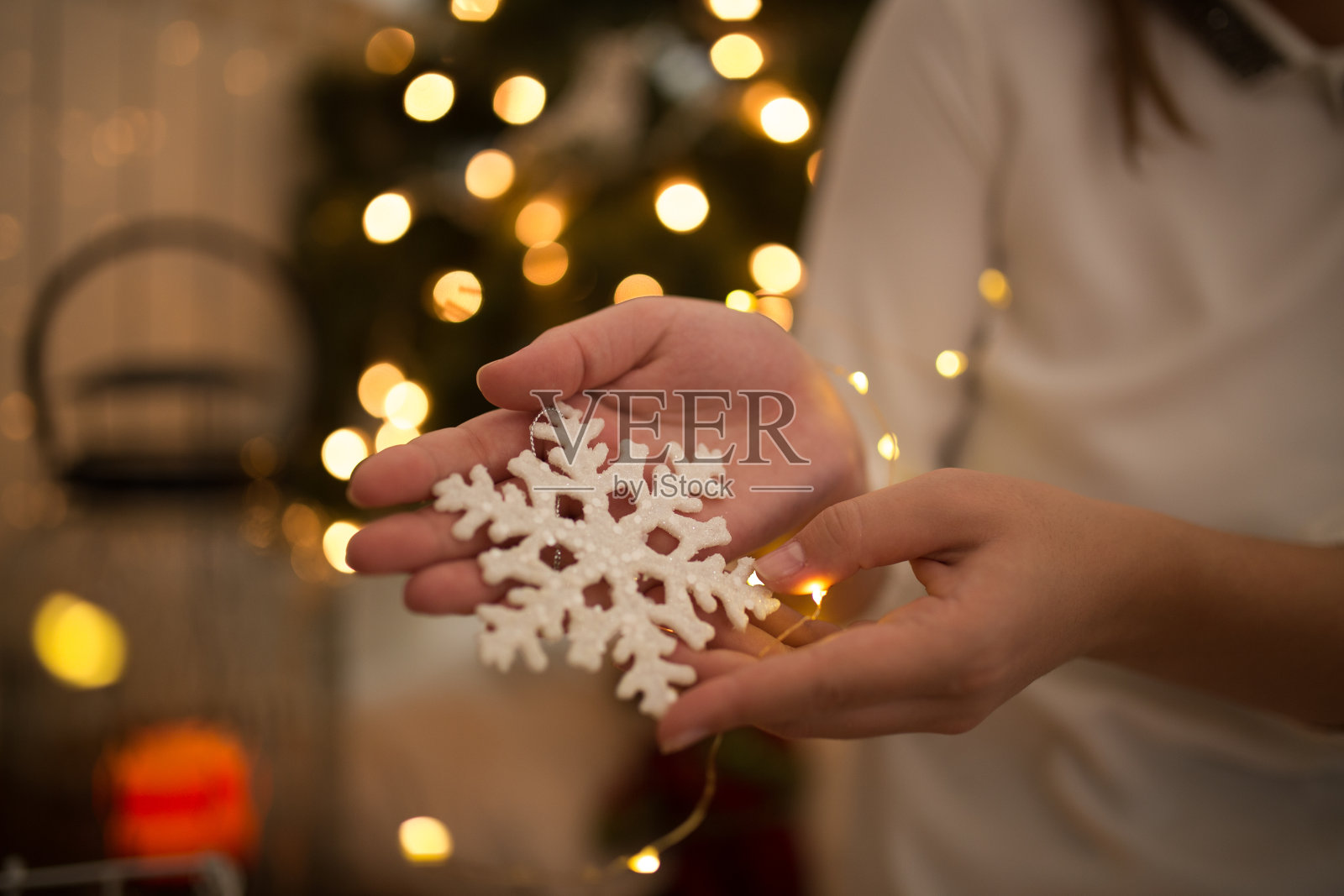 女人手捧着圣诞雪花装饰品，站在装饰着圣诞彩灯的圣诞树前照片摄影图片