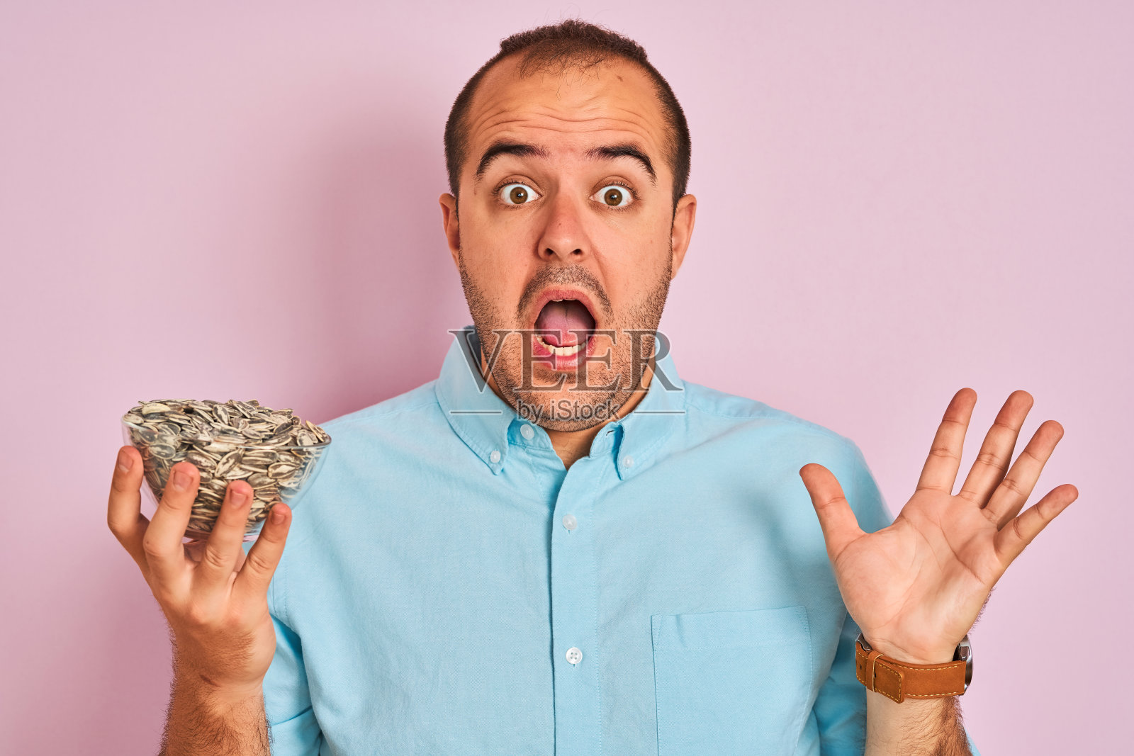 年轻人拿着碗葵花籽站在孤立的粉红色背景非常高兴和兴奋，胜利者的表情庆祝胜利尖叫着大大的微笑和举起手照片摄影图片