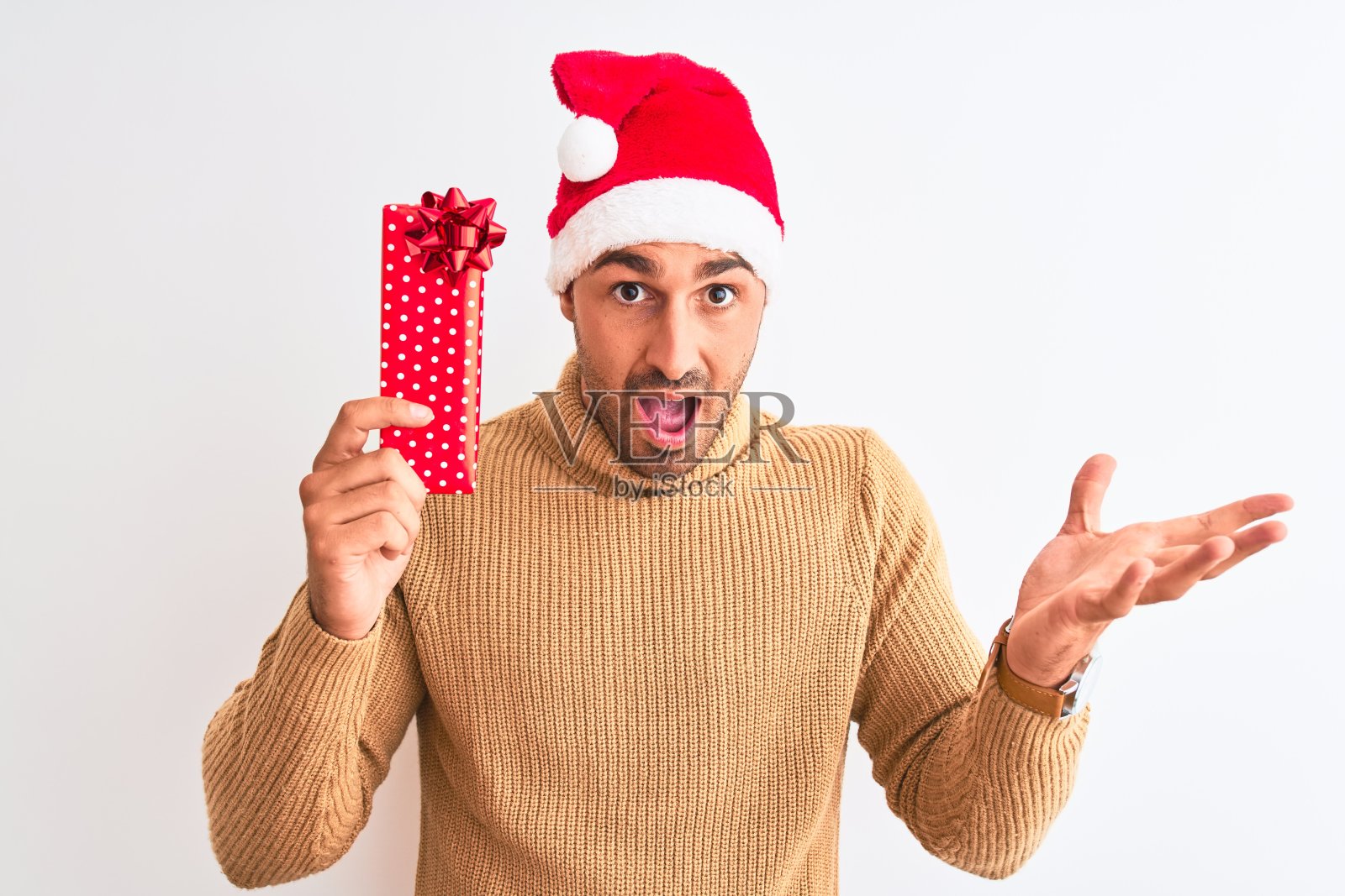 年轻英俊的男人戴着圣诞帽，拿着礼物越过孤立的背景非常高兴和兴奋，胜利者的表情庆祝胜利尖叫着大大的微笑和举起手照片摄影图片