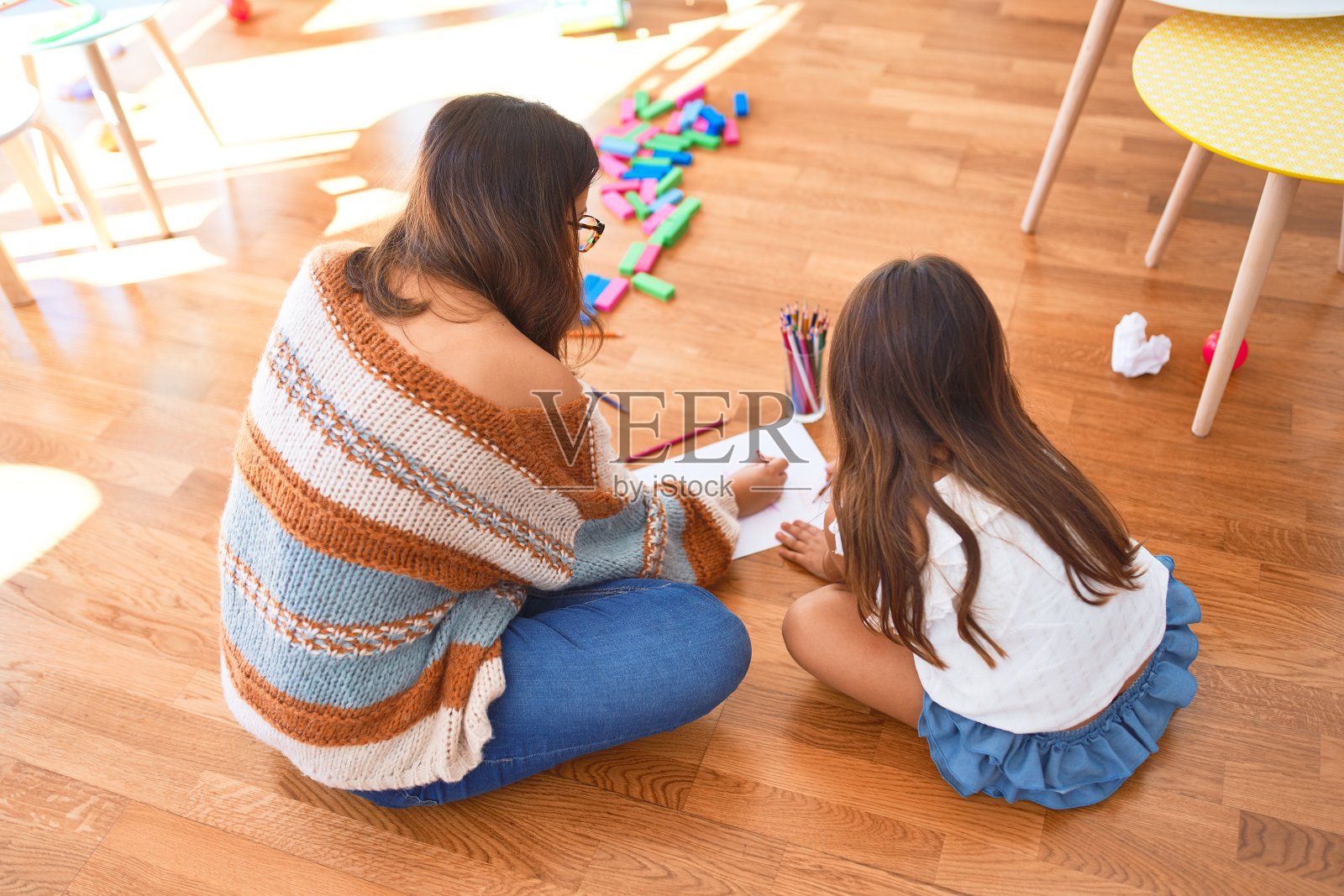 美丽的老师和幼童用铅笔和纸在幼儿园的玩具周围画画照片摄影图片