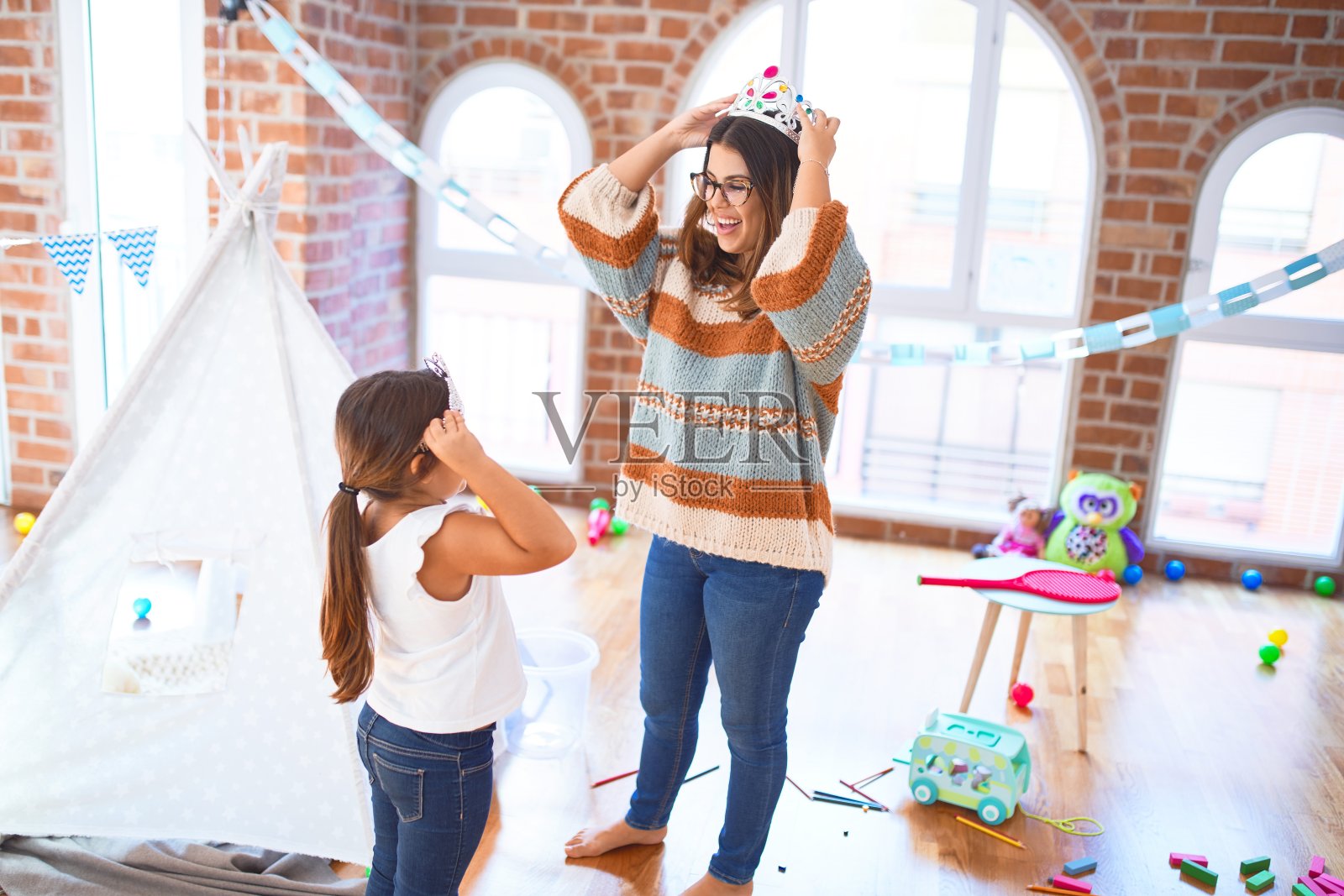 美丽的老师和孩子快乐地戴着公主皇冠在幼儿园的玩具照片摄影图片