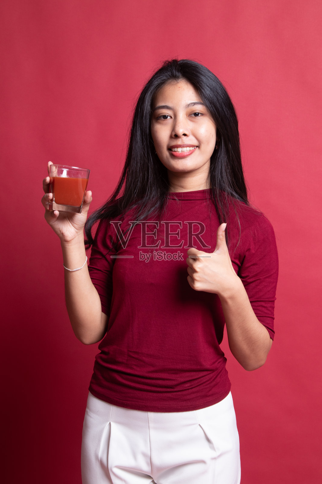 一位年轻的亚洲女性用番茄汁为自己竖大拇指。照片摄影图片