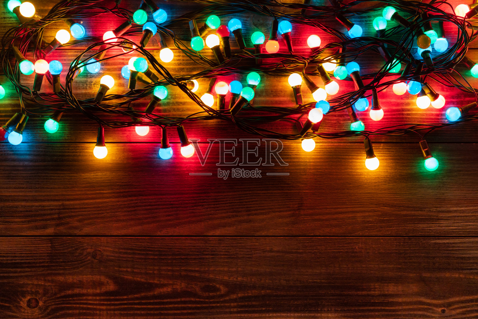 圣诞节的边界上有五颜六色的花环。深色木书桌上的圣诞背景照片摄影图片