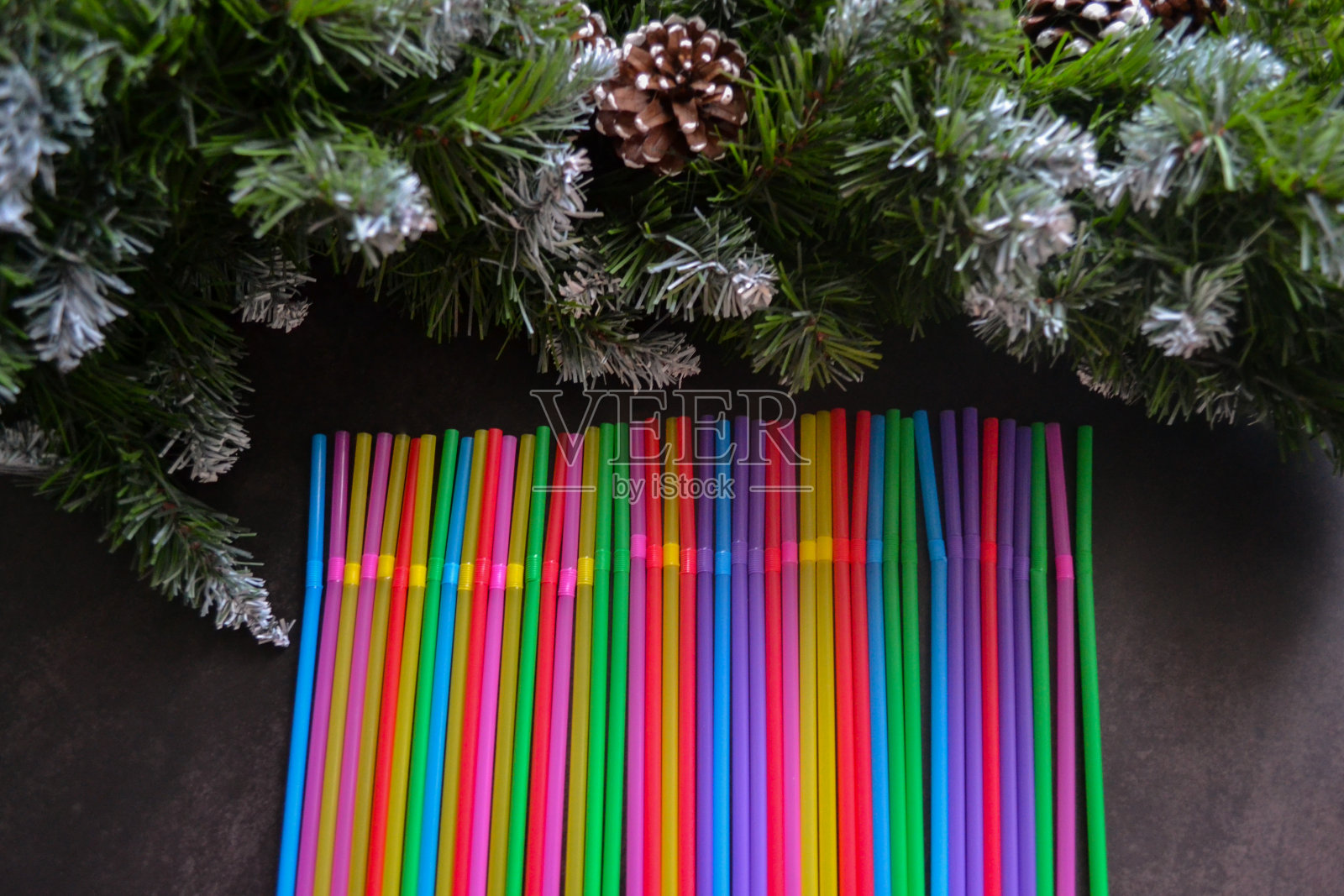 俯视图的多色塑料鸡尾酒吸管躺在一排。背景是带有球果的绿色云杉树枝。节日的背景。派对，新年和圣诞节的概念。本空间照片摄影图片