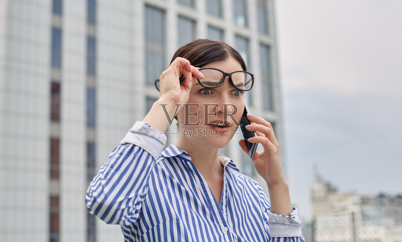 一个漂亮忙碌的女孩站在城市的背景上，正在用灰色的电话活跃地交谈照片摄影图片