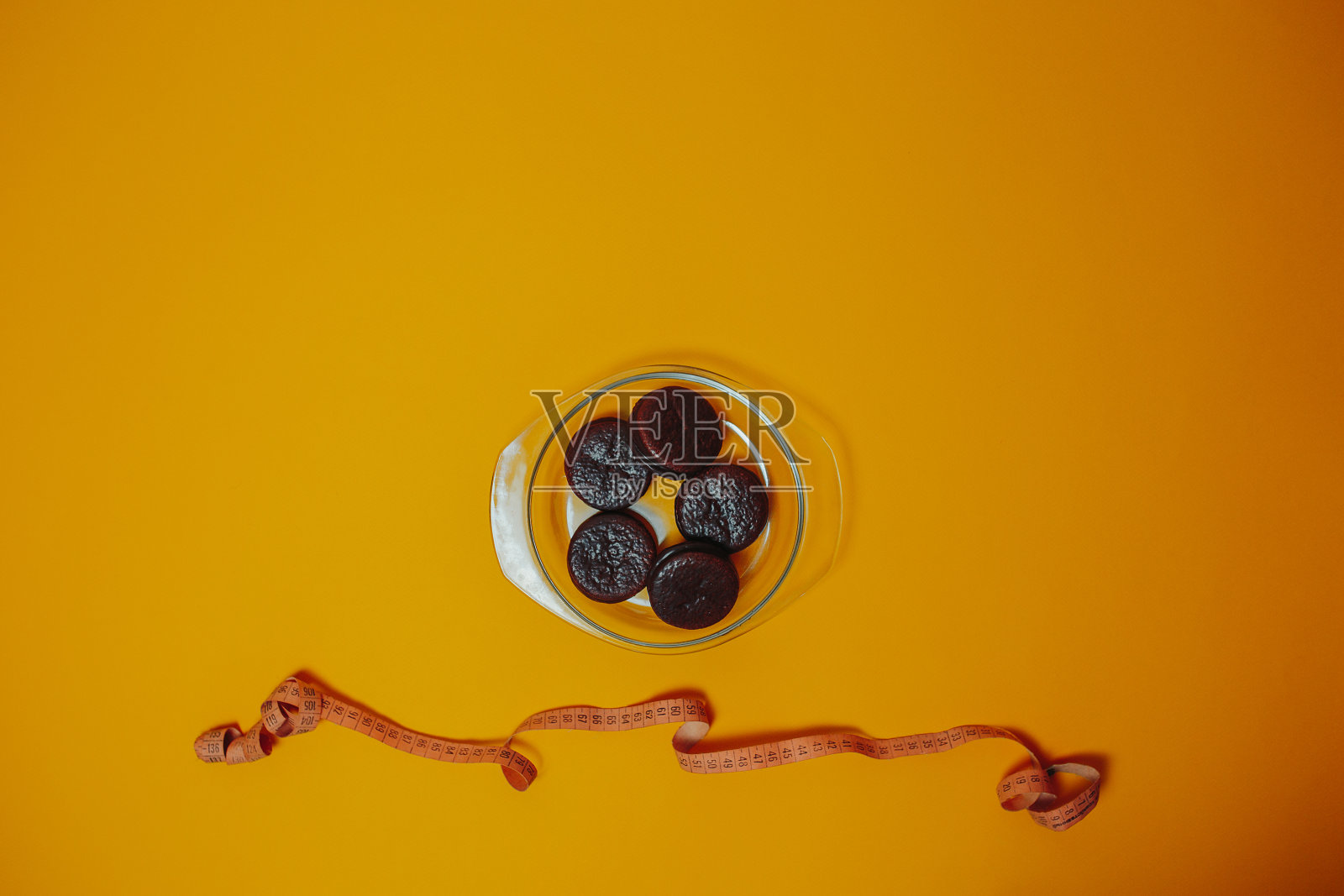 橙色背景上的饮食和减肥主题。用卷尺把巧克力蛋糕放在盘子里。照片摄影图片