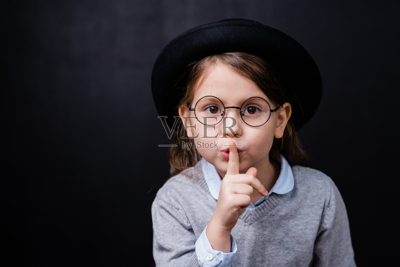 可爱的小女孩穿着漂亮的休闲装和眼镜要求你保持安静照片摄影图片