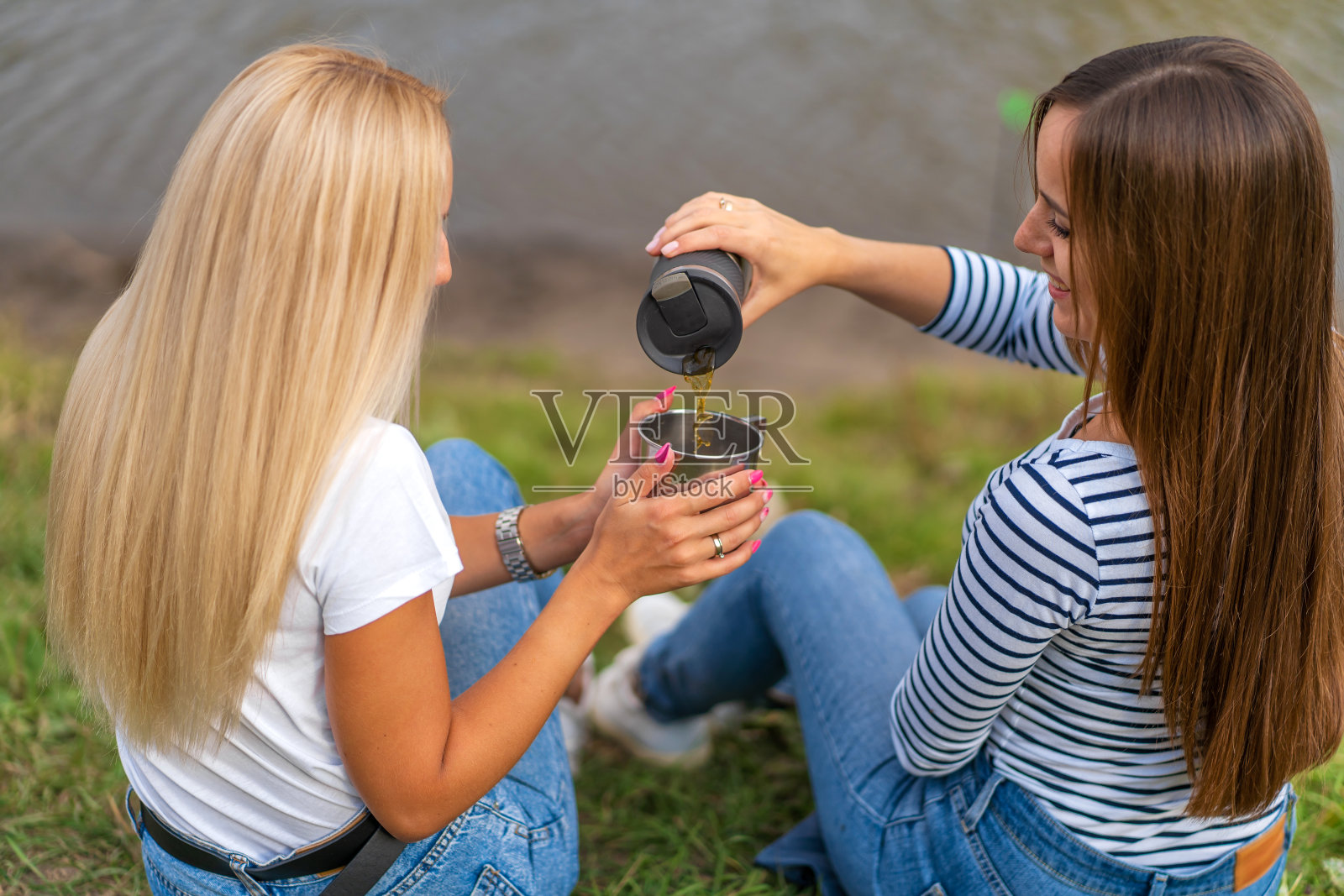 两个美丽的女孩在美丽的湖边享受自然，喝着热茶照片摄影图片