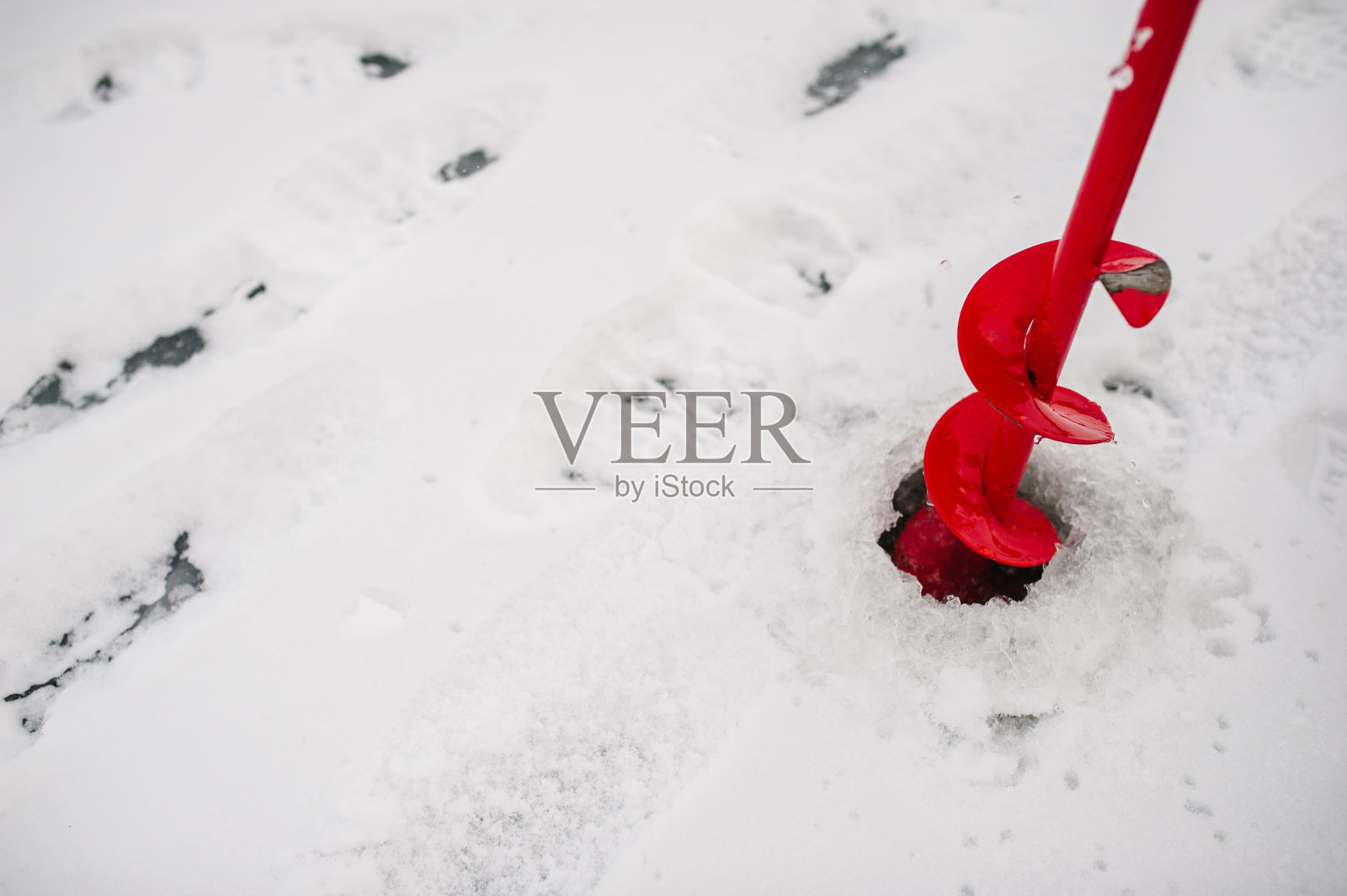 用螺丝钻个洞。渔网和钻头，螺丝，电动螺旋钻。冬天在结冰的湖面上钓鱼。冰。照片摄影图片