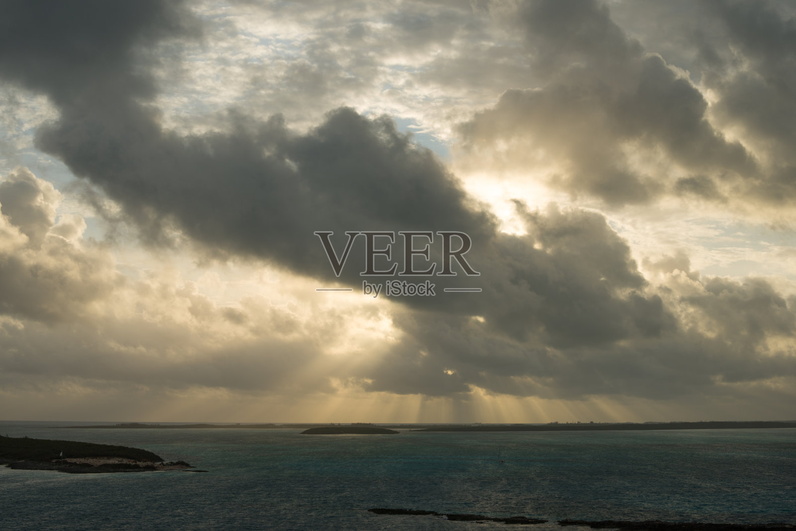 海面上戏剧性的多云天空——阳光穿透小岛上空的乌云照片摄影图片