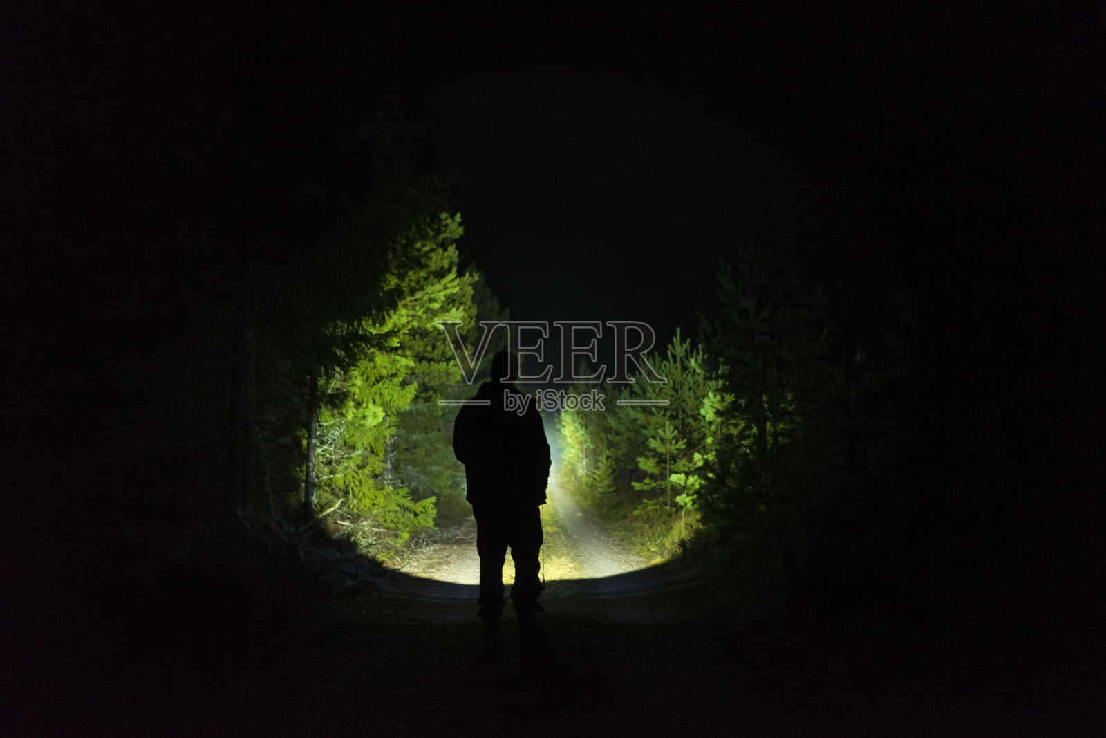 一个人站在户外，在黑暗的夜晚用手电筒发光照片摄影图片