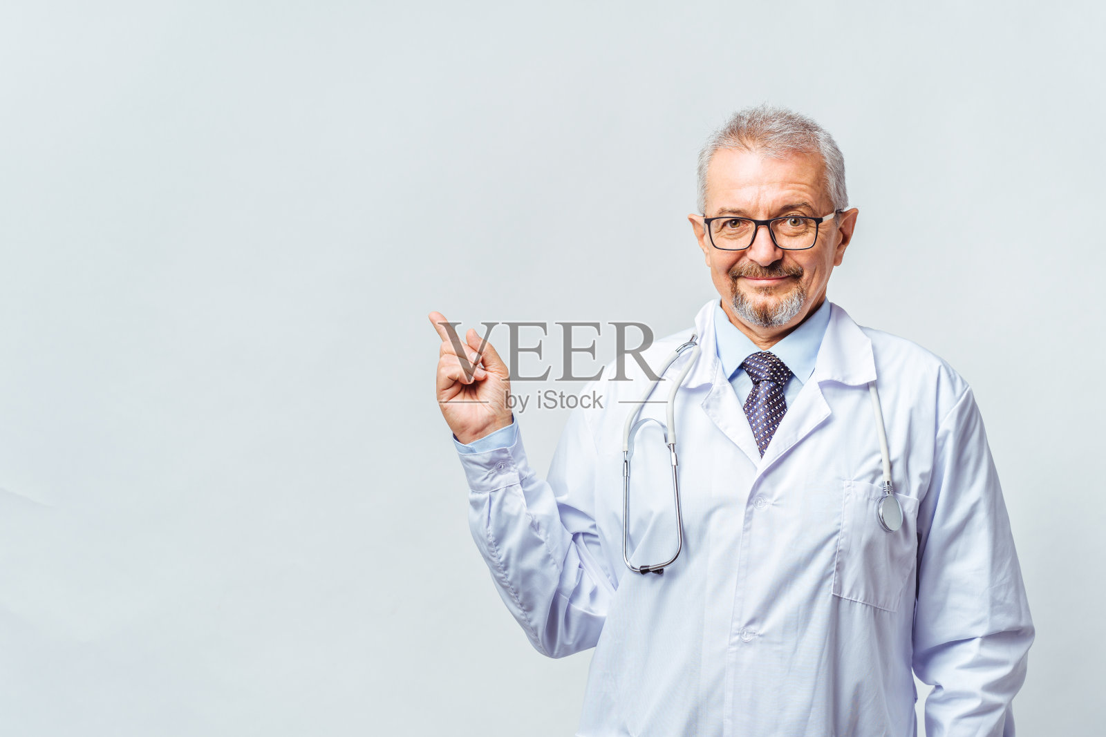 开朗成熟的医生在镜头前摆姿势和微笑，保健和医药。孤立在蓝色背景上。手指向拷贝空间照片摄影图片