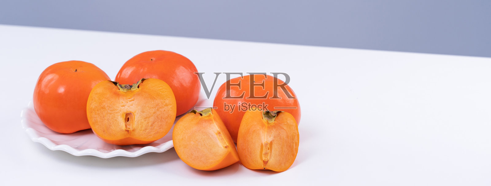 新鲜漂亮的切好的甜柿子卡吉孤立在白色的厨房桌子上，以灰蓝色为背景，中国农历新年设计理念，近距离。照片摄影图片