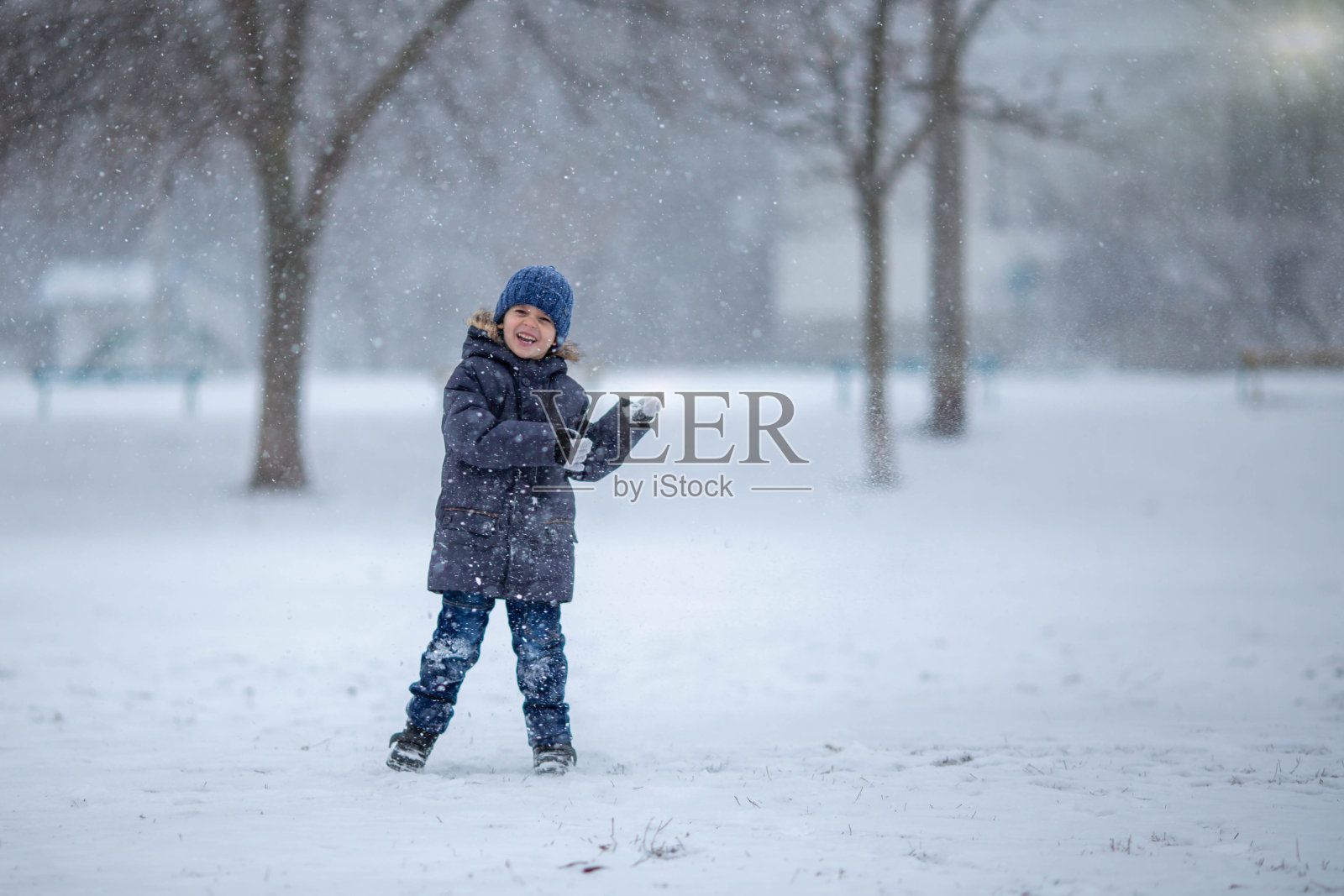 一个戴着帽子、穿着夹克的小男孩在冬天的雪地里笑着、快乐着。照片摄影图片