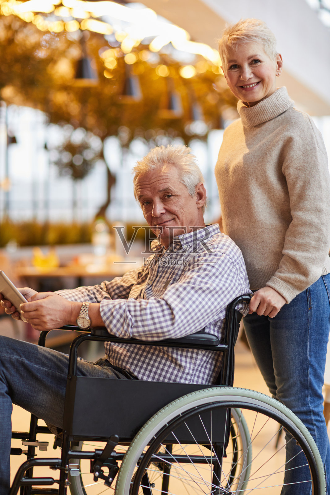 欢快小心成熟的妻子的肖像在毛衣推轮椅与丈夫使用数字平板电脑照片摄影图片